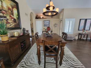 A dining room with a wooden table, chairs, a chandelier, and a large painting on the wall.