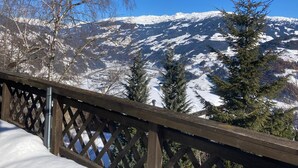 Una terraza de madera con vistas a montañas nevadas y árboles de hoja perenne.