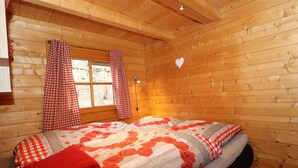 Una habitación de cabaña de madera con una cama, cortinas de cuadros y una ventana.