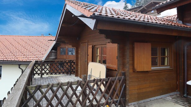 Una cabaña de madera con techo de tejas, un balcón de madera con barandilla de celosía y una ventana con contraventanas de madera.