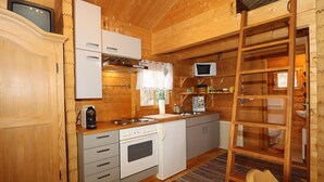 Una cabaña de madera compacta con kitchenette, que incluye estufa, microondas y armarios.