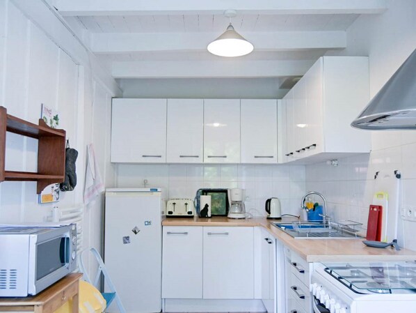 A compact kitchen with white cabinets, a microwave, a toaster, a kettle, and a gas stove.