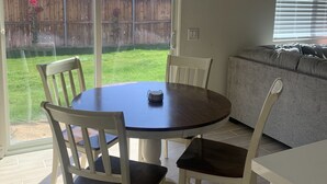 Un coin repas avec une table ronde et des chaises, un luminaire au plafond et une porte-fenêtre coulissante donnant sur un jardin.
