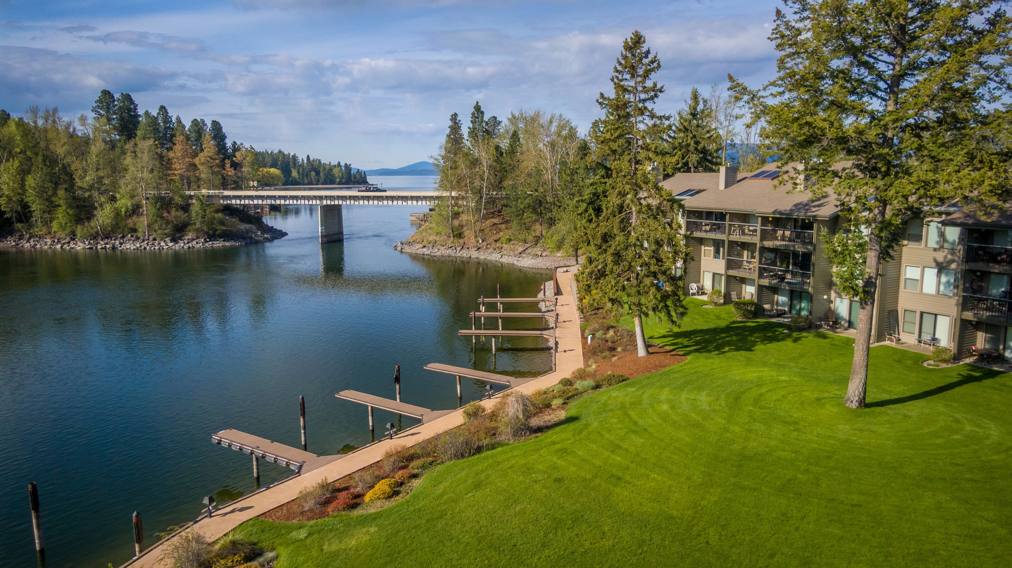 A lakeside view of a multi-story building with a dock and a bridge in the background.