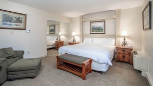 Camera d'albergo con un letto grande, una panca in legno, un tavolino e un comodino con una lampada.