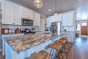 A modern kitchen with white cabinets, a granite countertop, stainless steel appliances, and wooden bar stools. - 3BR Rellerstone Bunkhouse w/AC Fall Special - buy 5 nights, get 2 free Sept. - Nov (Victor)