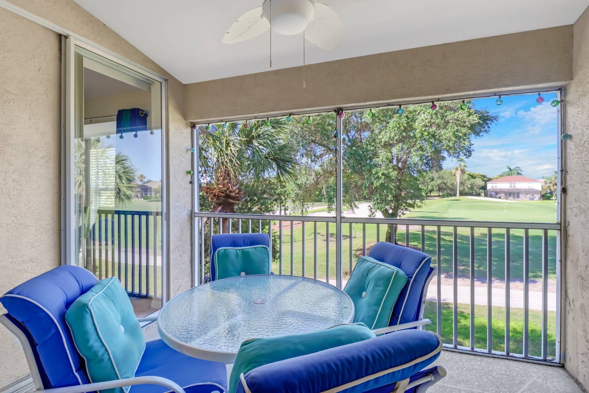 A balcony with a glass table and blue chairs, overlooking a golf course.