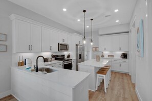 Une cuisine moderne avec des meubles blancs, des appareils en acier inoxydable et des luminaires suspendus.