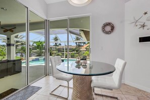 A modern room with a glass door leading to a pool area, a round glass table with chairs, and a decorative wreath on the wall.