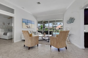 A spacious living area with a large window, a sofa, two wicker chairs, and a coffee table.