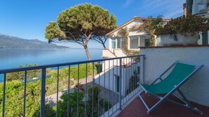 A balcony with a green chair, a tree, and a view of a lake and mountains.