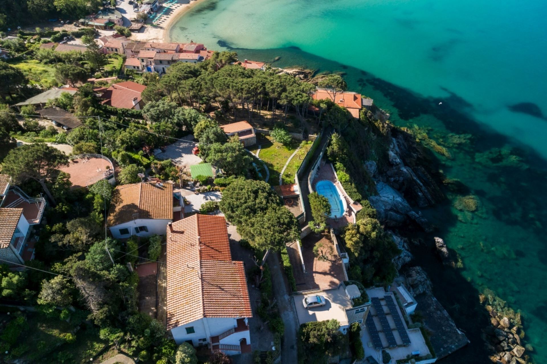 An aerial view of a coastal residential area with houses, a swimming pool, and a beach.