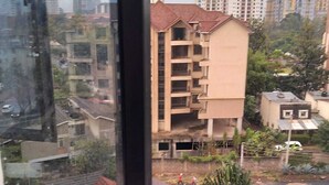 A view from a window overlooking a residential area with multi-story buildings, some under construction, and a few pedestrians in the distance. - Stay.Plus Hurlingham Business Apartment (Nairobi)
