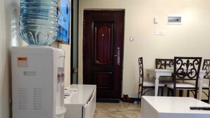 A compact living space with a kitchenette, a dining area with a table and chairs, and a water dispenser. - Stay.Plus Hurlingham Business Apartment (Nairobi)