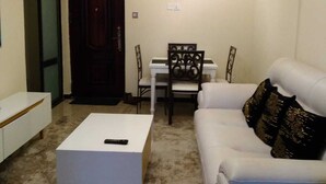 A living room with a white sofa, a white coffee table, a dining table with chairs, and a chandelier. - Stay.Plus Hurlingham Business Apartment (Nairobi)