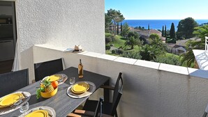 A dining table set with yellow plates, a bottle, and a pineapple on a balcony overlooking a coastal view. - Le Village (C5 235) by Interhome (Agay Village Cap Esterel)