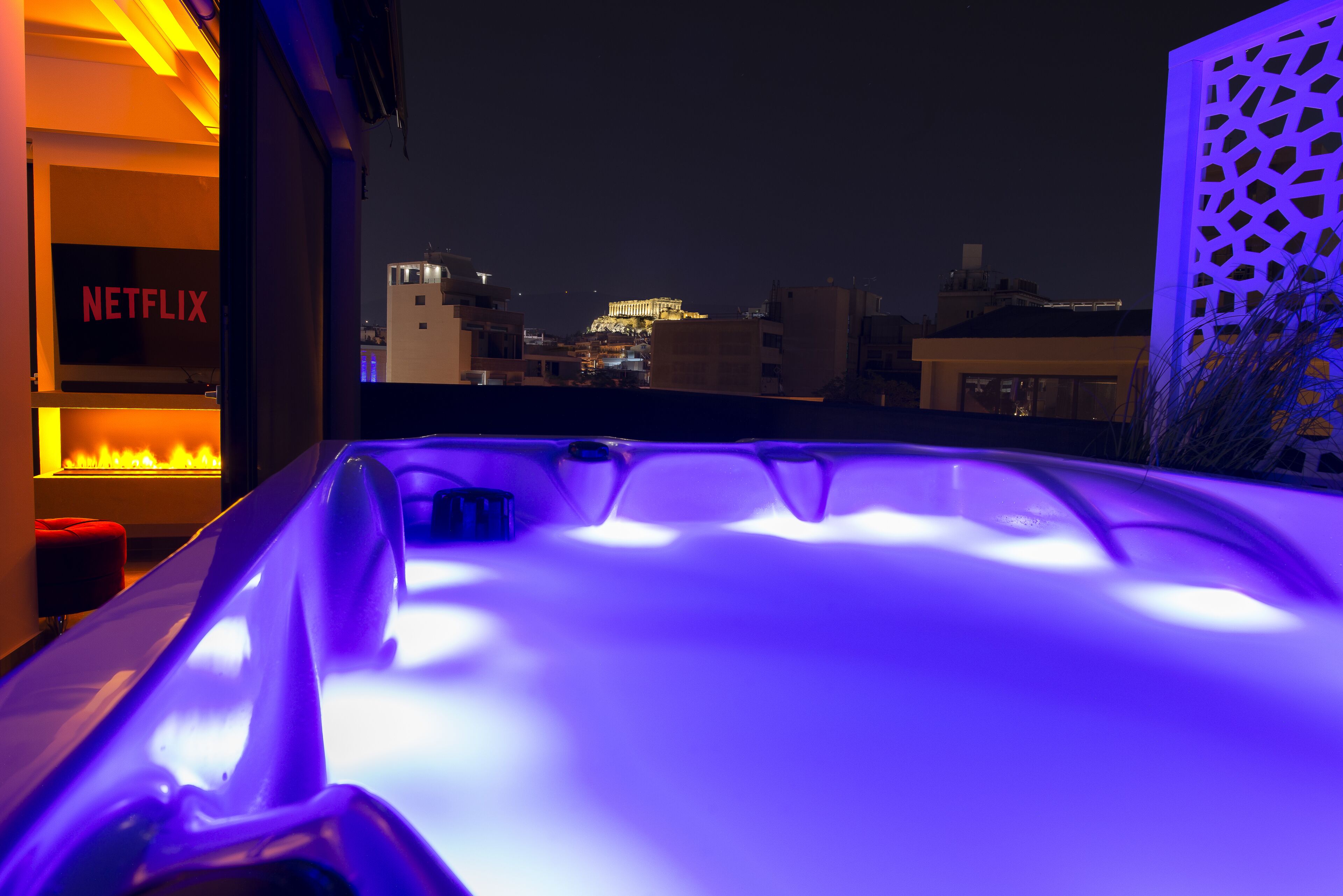 A hot tub with a view of a cityscape at night, including a building with a sign that reads "NETFLIX".