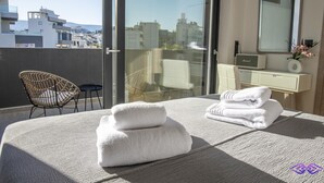 Ein modernes Hotelzimmer mit Bett, Stuhl, Schminktisch mit Spiegel und Blick auf die Stadt durch große Fenster.
