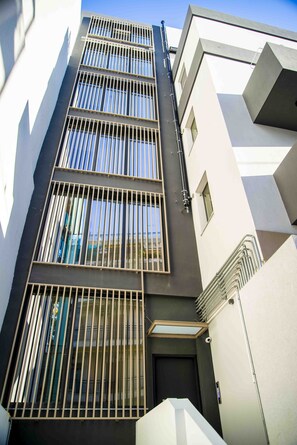 A modern building with multiple floors, large windows with metal bars, and a clean, geometric architectural design.