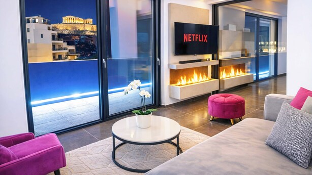 Ein modernes Wohnzimmer mit Fernseher, Kamin und Blick auf eine Stadtlandschaft.