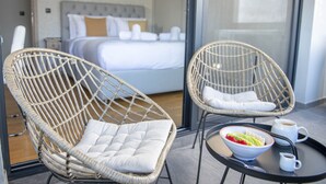 Ein Hotelzimmer mit einem Bett, zwei Korbstühlen, einer Ablage mit einer Fruchtschale und einer Kaffeetasse.