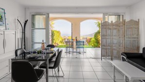 A modern dining area with a glass table, black chairs, and a view of a garden through an open archway. - Les Bastides (O4 023) by Interhome (Agay Village Cap Esterel)