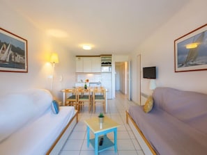 Ein kompaktes Hotelzimmer mit Bett, Sofa, kleinem Tisch, Fernseher und einer Küchenzeile im Hintergrund.