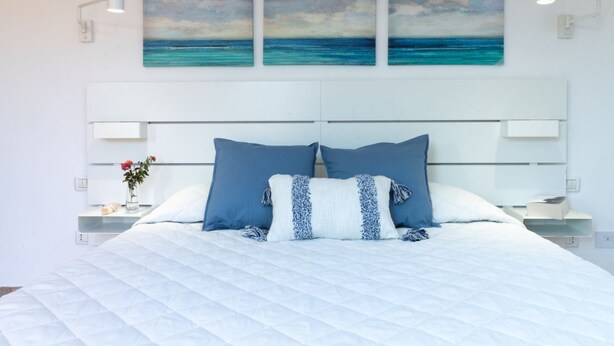 A bedroom with a large bed, white headboard, and three wall-mounted paintings of a seascape.