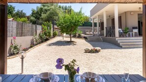 An outdoor patio with a table set for dining, surrounded by a gravel area and a small tree.