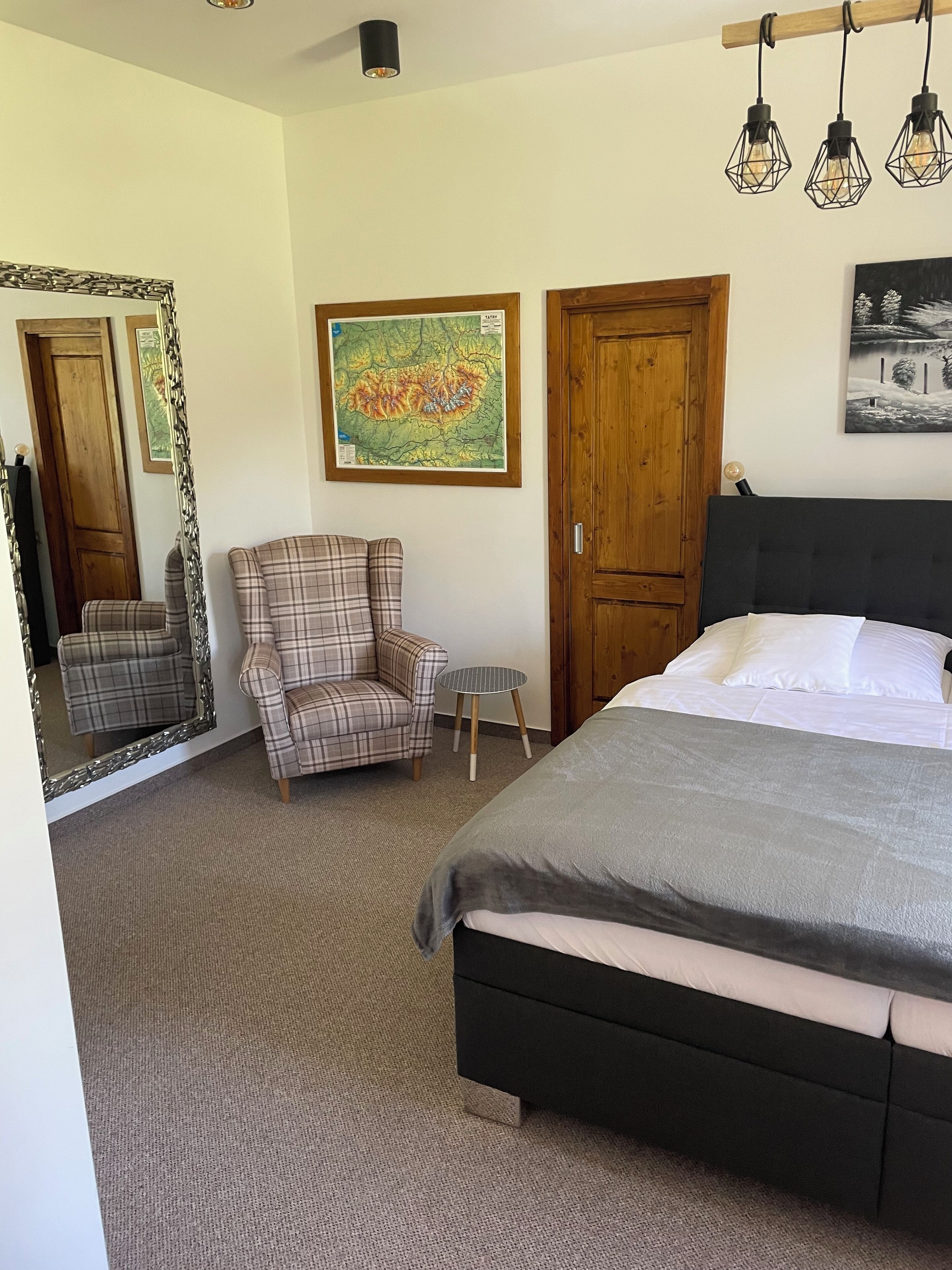 A bedroom with a large bed, a chair, a small table, a mirror, and a map on the wall.