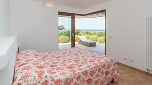 Ein Schlafzimmer mit Bett, Blick ins Freie und einer Schiebetür zum Balkon.