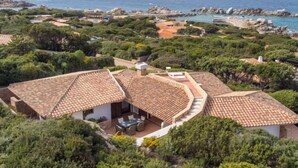 Ein Küstenanwesen mit terrakottafarbenen Dächern, einer Terrasse mit Gartenmöbeln und Blick auf das Meer und die felsige Küste.