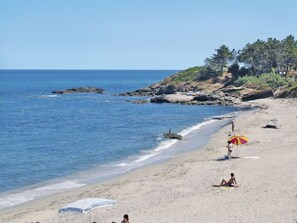 Ein Strand mit klarem, blauem Wasser, Felsformationen und ein paar Menschen, die unter Sonnenschirmen entspannen.