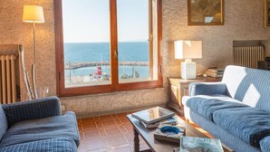 A cozy living room with a large window overlooking the sea, a fireplace, and two sofas.