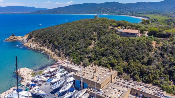 A coastal property with a marina, a hilltop house, and a view of the sea and mountains.