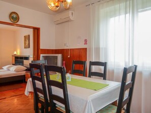 A hotel room with a bed, a desk, a chair, a table with a green placemat, and a window with curtains.