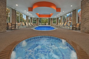 Un espace piscine intérieure doté d’un jacuzzi, de chaises longues et d’un mur en briques.