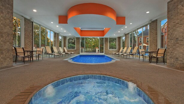 Zona de piscina interior con jacuzzi, sillas de descanso y vistas a árboles a través de amplios ventanales.