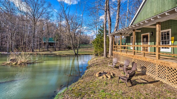 A cabin with a wooden deck overlooking a calm lake, surrounded by trees. - Bright ‘Green Gables’ Cabin: Hike, Swim & BBQ (Lewisburg)