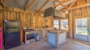 Une cuisine rustique aux murs en bois, avec un réfrigérateur noir, un four et une grande cheminée.
