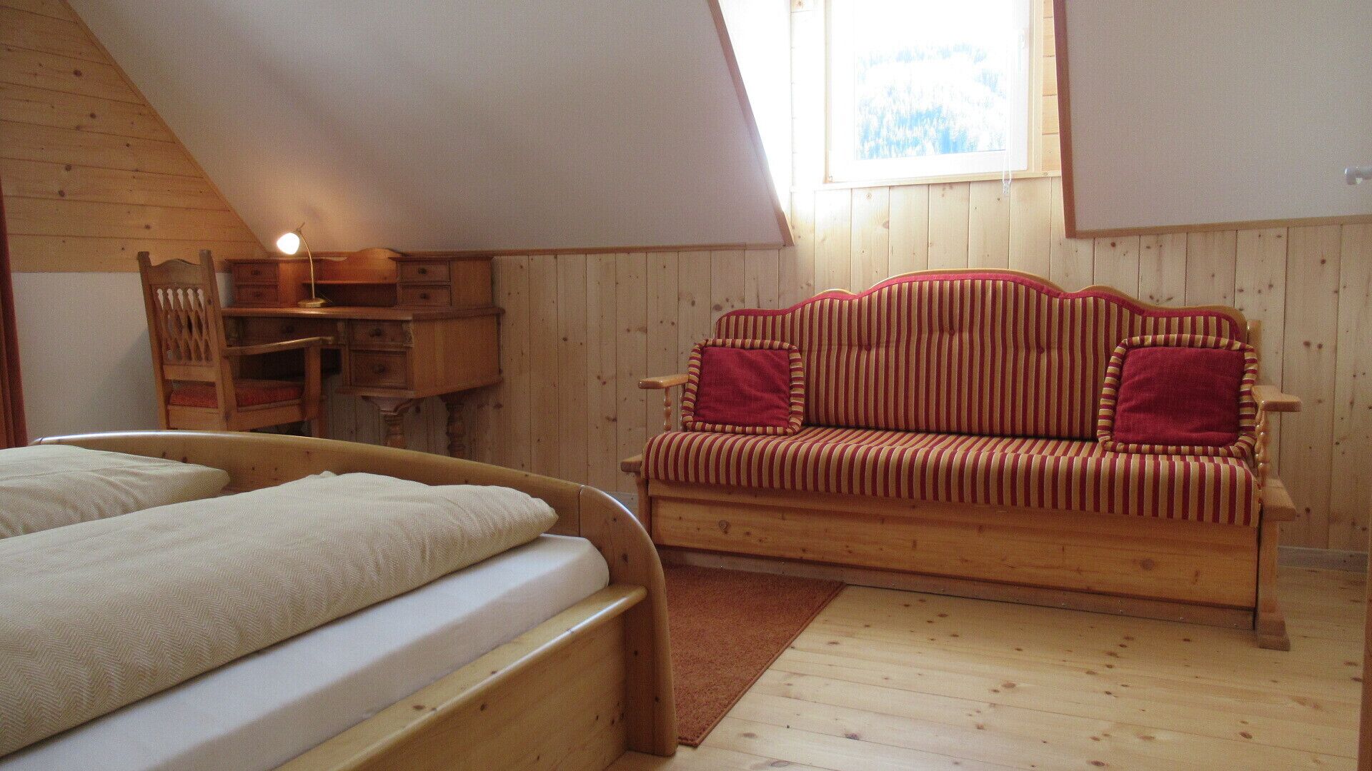 Ein gemütliches Zimmer mit einem hölzernen Bett, einem gestreiften Sofa und einem Schreibtisch mit Lampe.