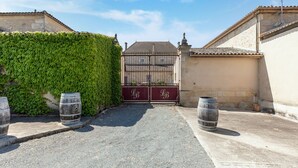 A gated courtyard with a paved path, a hedge, and two barrels. - Elegant Château Escape (Cezac)