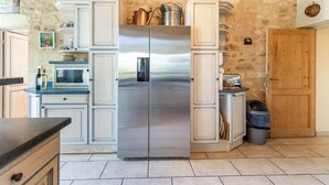A kitchen with a stainless steel refrigerator, white cabinetry, and a stone wall. - Elegant Château Escape (Cezac)