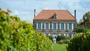 A large, two-story stone building with a red-tiled roof and white shutters, surrounded by well-maintained greenery. - Elegant Château Escape (Cezac)