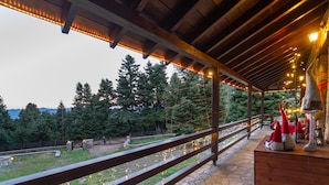 Un espacio al aire libre techado con suelo de piedra, barandas de madera y luces colgantes.