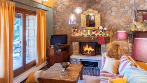 Una sala de estar acogedora con chimenea de piedra, techo de madera y televisor.