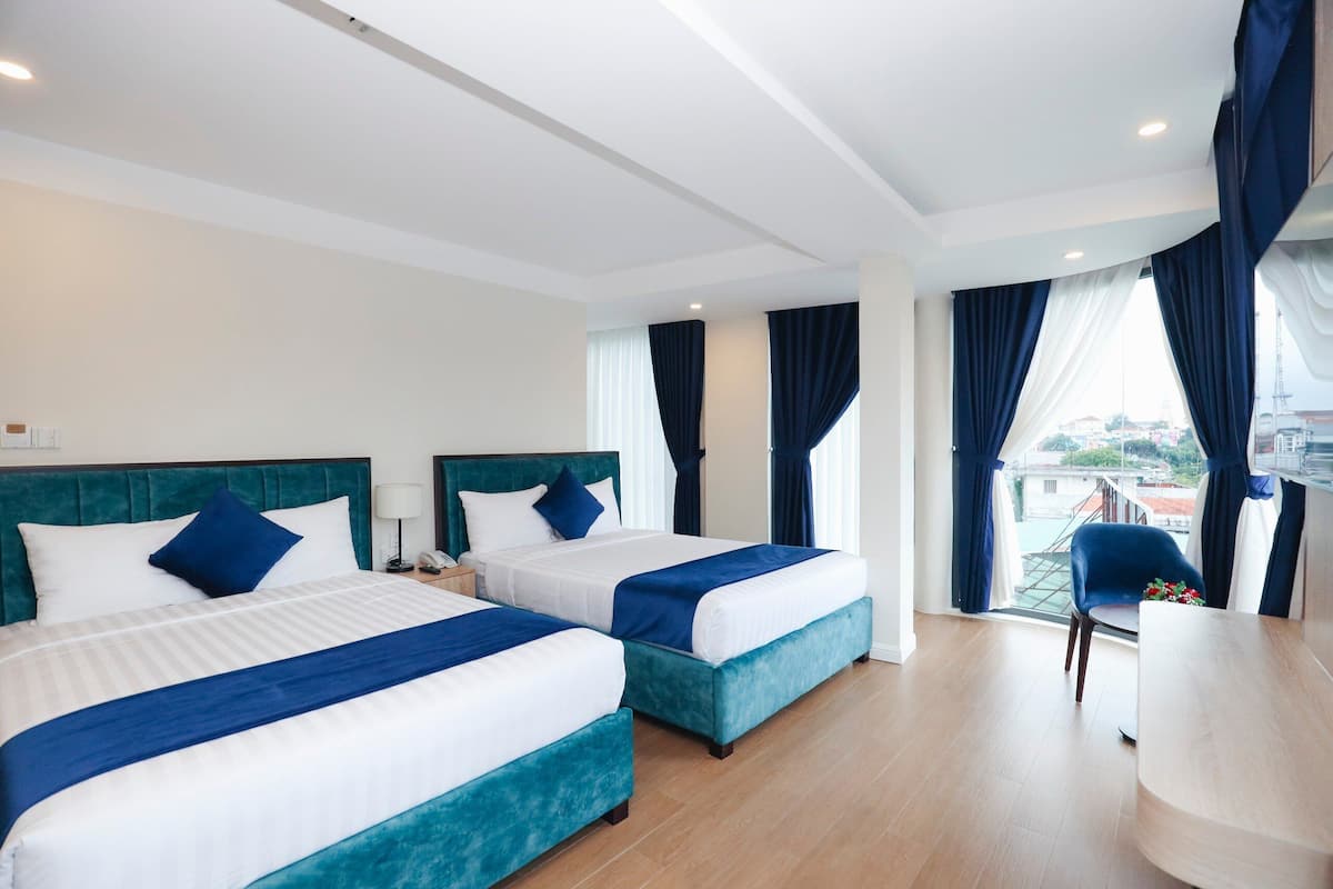 A hotel room with two beds, a desk, and a view of the city.