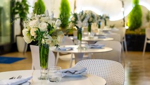 A dining area with round tables and white chairs, each set with plates, cutlery, and a vase of flowers. - Sandals Flora Hotel (Xuan Huong - Da Lat)