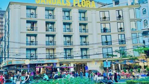 A hotel named "SANDALS FLORA" with multiple floors, balconies with plants, and a ground-level restaurant named "L'ANGFARM". - Sandals Flora Hotel (Xuan Huong - Da Lat)