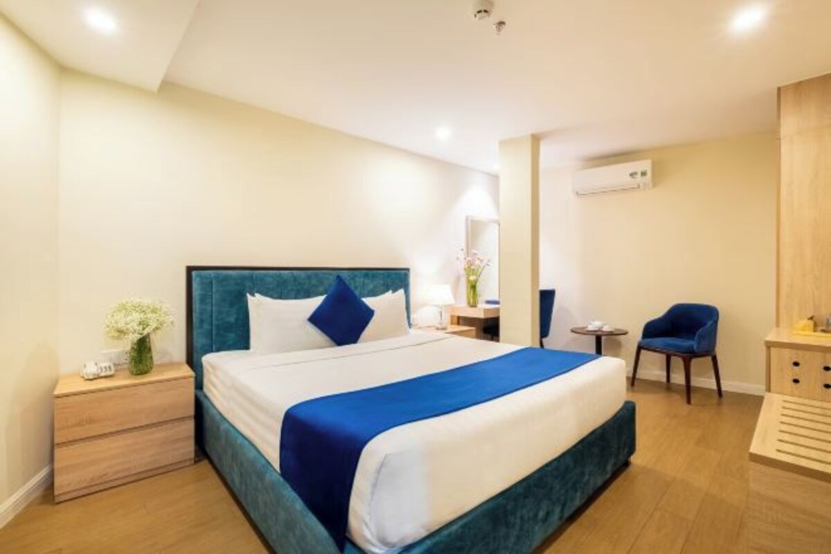 Una habitación de hotel con una cama grande, mesitas de noche, una silla y un armario.